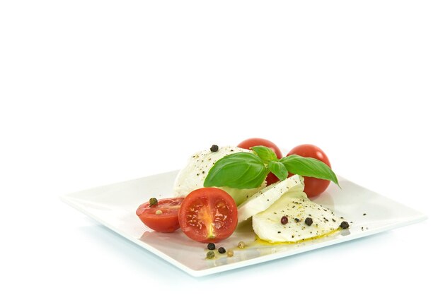 Delikatesse der italienischen Küche Mozzarella-Käse mit Basilikumblättern und Babytomaten, gewürzt mit Olivenöl und Pfeffer, isoliert auf weißem Hintergrund mit Platz für Werbetext