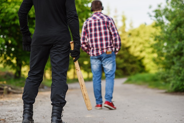 Un delincuente vestido de negro con un bate de béisbol en sus manos ataca a un hombre. Robar en la calle durante el día.