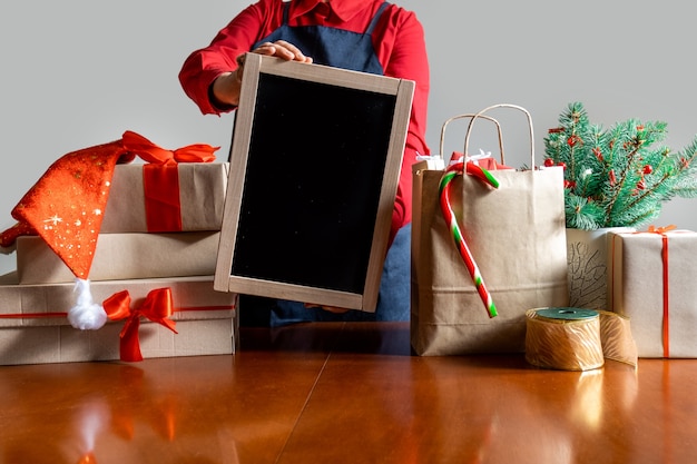 Deliver's Hands Hold Shopping Board in der Nähe von Packtasche, Geschenkboxen und Weihnachtsbaum.