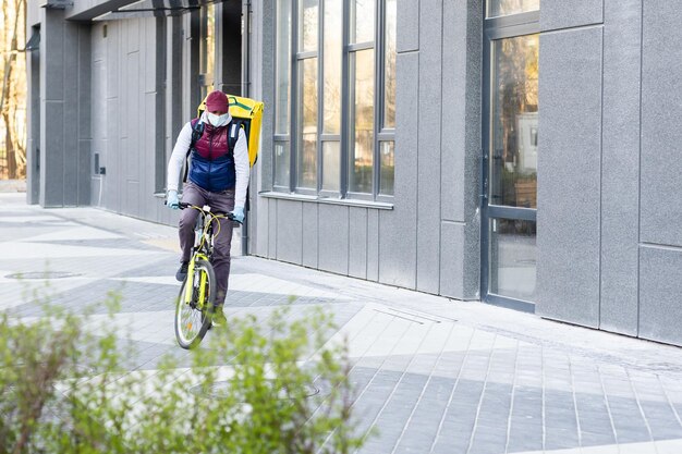 Delivery Man steht mit gelbem Thermo-Rucksack für die Lieferung von Lebensmitteln in der Nähe des Eingangs nach Hause mit leerem Platz zum Kopieren und Einfügen.