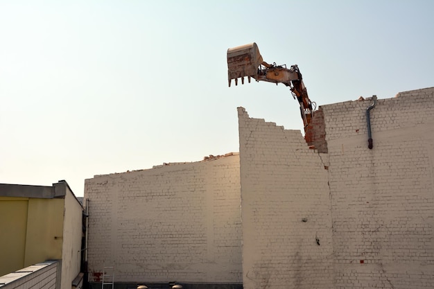 Demolición de una pared de ladrillos de un edificio antiguo usando un cucharón de excavadora Desmantelamiento de la ciudad