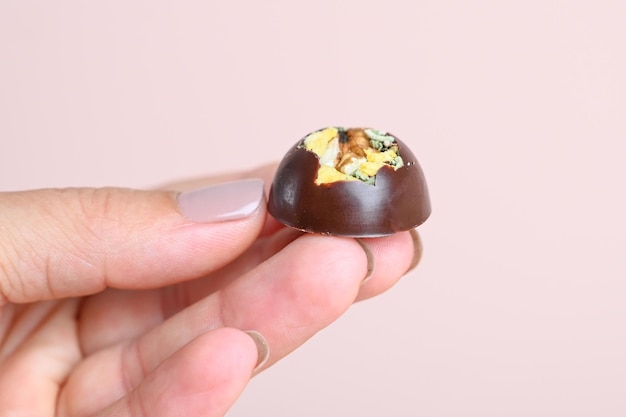 Demostración de caramelos de chocolate con relleno de nueces o frutas en los dedos extendidos de una mano femenina con manicura