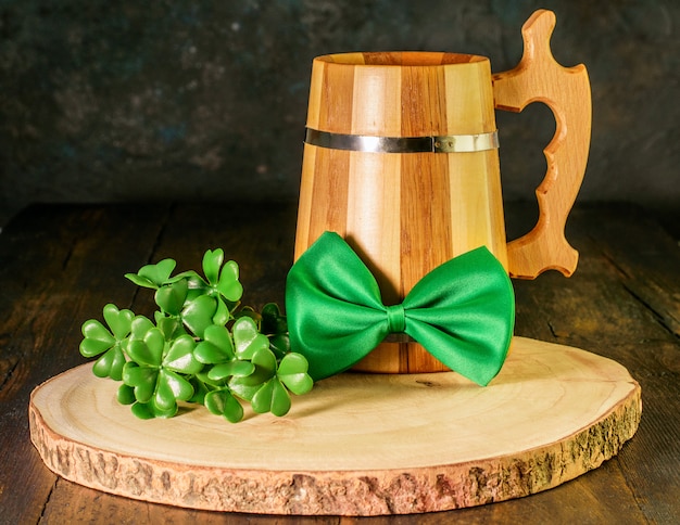 Den St. Patrick Day feiern. Holzkrug grünes Bier, grüne Fliege und ein Zweig Kleeblatt auf Naturholz