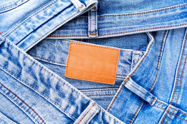 Denim-Textur, ein Haufen Blue Jeans und ein leeres Lederetikett in Nahaufnahme, eine Vielzahl bequemer Freizeithosen und -kleidung