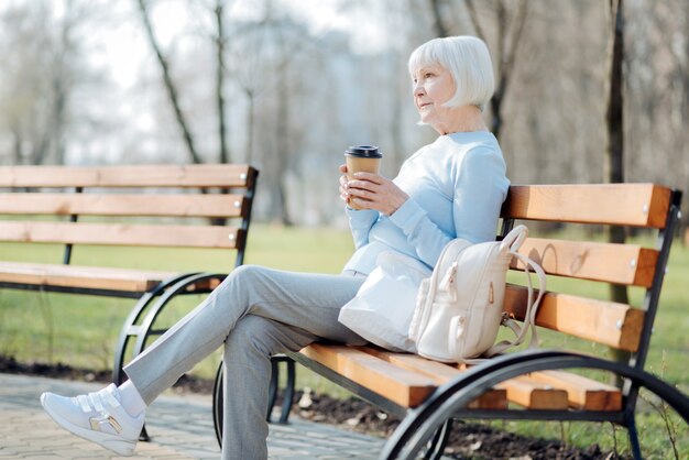 Denken. Nachdenkliche blonde Frau, die Kaffee trinkt, während sie auf der Bank sitzt