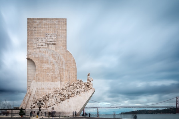 Denkmal für die Entdeckungen (Pedrao dos Descobrementos) am Nordufer des Tejo in Lissabon, Portugal, mit der Brücke vom 25. April im Hintergrund.