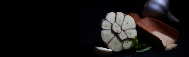 Dente de alho fresco em fundo preto. o alho é rico em vitaminas, primavera útil, bons temperos. alho cortado em um fundo escuro. alho fatiado cru.