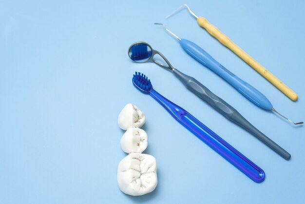 Foto dentes artificiais com cárie e escova de dentes com utensílios odontológicos em um azul