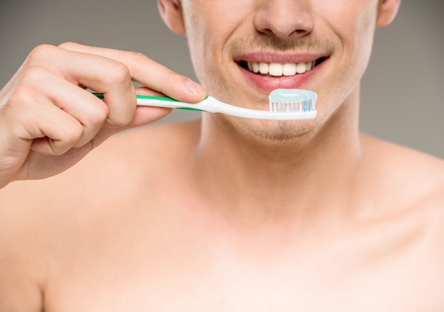 Dentes consideráveis da limpeza do homem com a escova de dentes no banheiro.