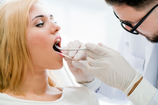 Dentes de exame do dentista considerável novo do paciente feliz da mulher na cadeira do dentista na clínica dental.