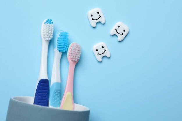 Dentes de plástico com rostos fofos e escovas de dentes em plano de fundo azul claro Espaço para texto