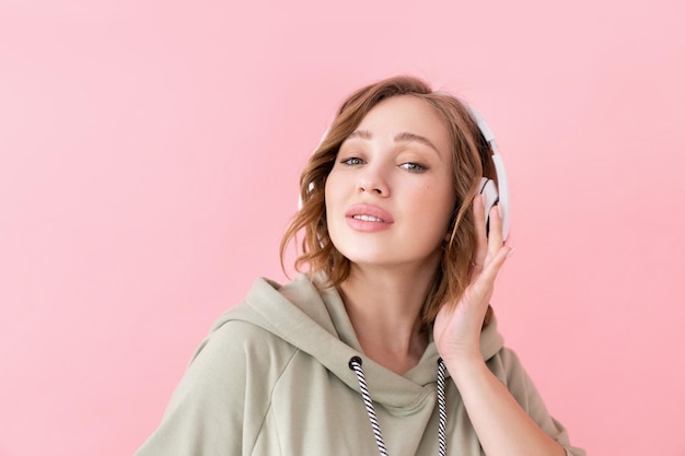 Dentes felizes sorriem mulher ouve música fones de ouvido Mulher caucasiana gosta de podcast ou livros de áudio vestido com capuz grande fundo rosa close-up retrato