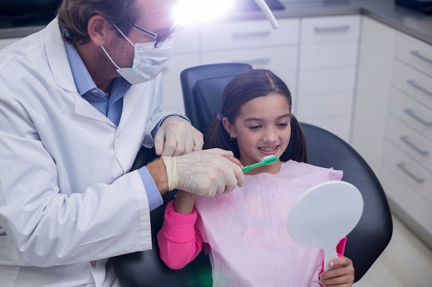 Dentista, ajudando o jovem paciente enquanto escova os dentes