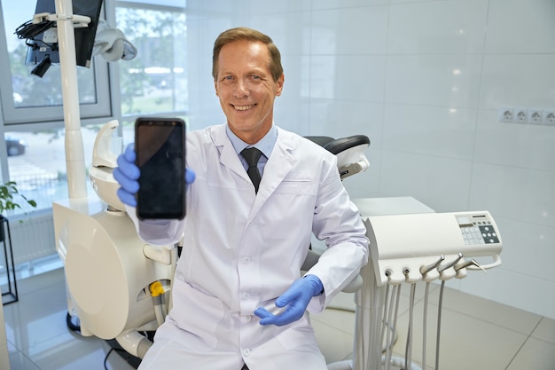 Dentista amigável segurando um smartphone com tela em branco