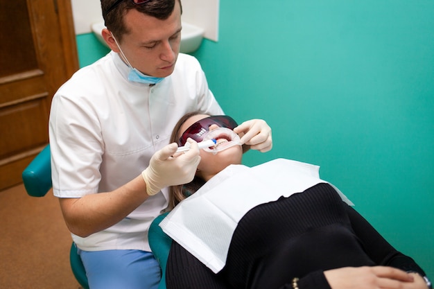El dentista aplica un gel para blanquear los dientes con una jeringa. Niña se somete a un procedimiento de blanqueamiento dental en una clínica dental