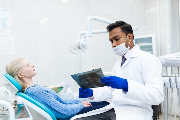 Dentista asiático masculino no consultório odontológico, conversando com uma paciente do sexo feminino e se preparando para o tratamento. equipamento médico moderno