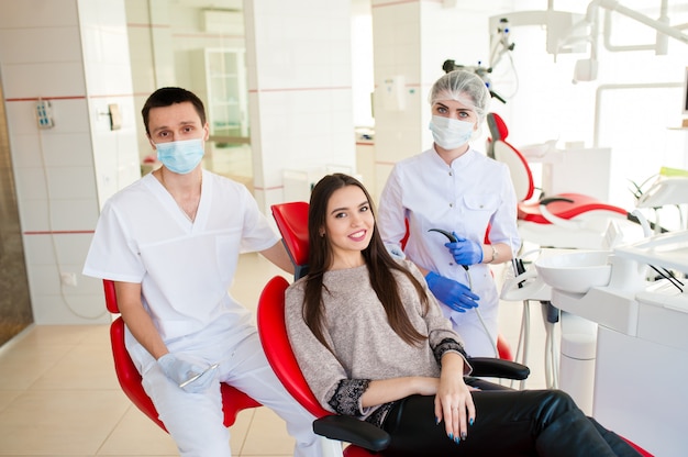 Un dentista con un asistente, cura los dientes a una hermosa niña.