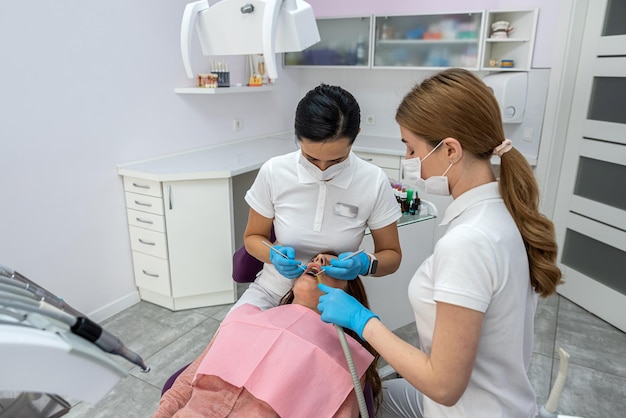 Una dentista con una asistente diagnostica y trata los dientes de una nueva paciente