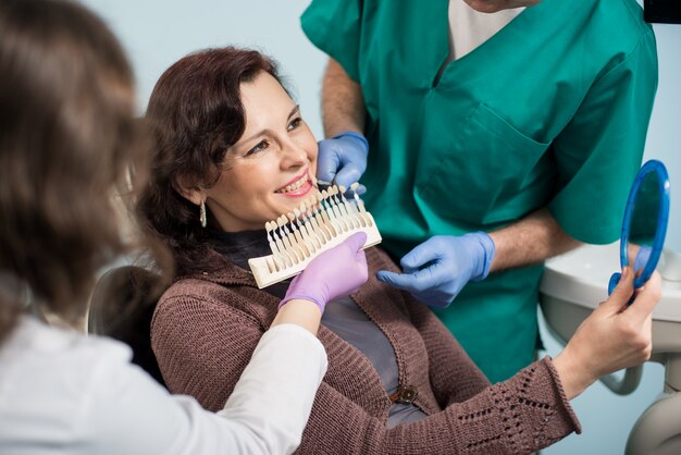 Dentista con asistente y paciente femenino comprobando y seleccionando el color de los dientes en la oficina de la clínica dental.