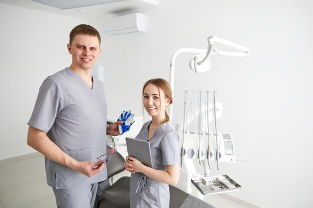 Dentista y asistente en la sala de examen sonriendo