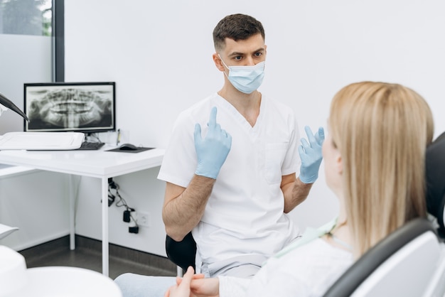 Dentista atraente em uma máscara protetora se comunica com um paciente atraente. o dentista trabalha no consultório odontológico