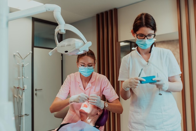 Un dentista con la ayuda de un colega realiza una operación en la mandíbula de un paciente anciano en una clínica dental moderna. foto de alta calidad