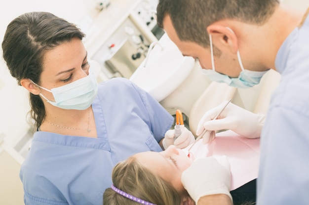 Dentista y ayudante dental que examinan los dientes de la chica joven