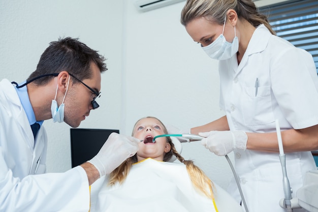 Dentista con ayudante examinando dientes de chicas