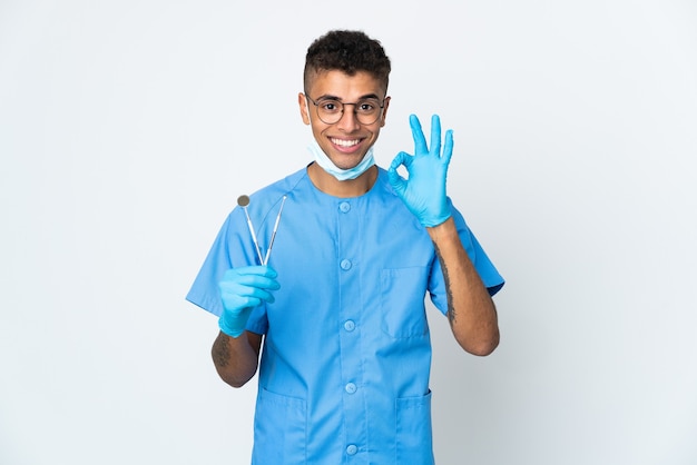 Dentista brasileño sujetando la herramienta aislada sobre fondo blanco mostrando signo de ok con los dedos