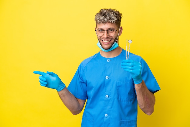 Dentista, caucásico, hombre, tenencia, herramientas, aislado, en, fondo amarillo, señalar con el dedo, hacia, el, lado