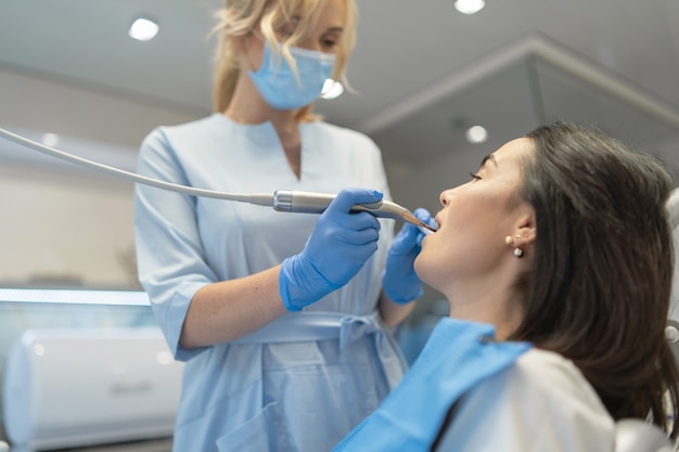 Dentista en la clínica dental que proporciona examen y tratamiento de la cavidad bucal para el paciente femenino.