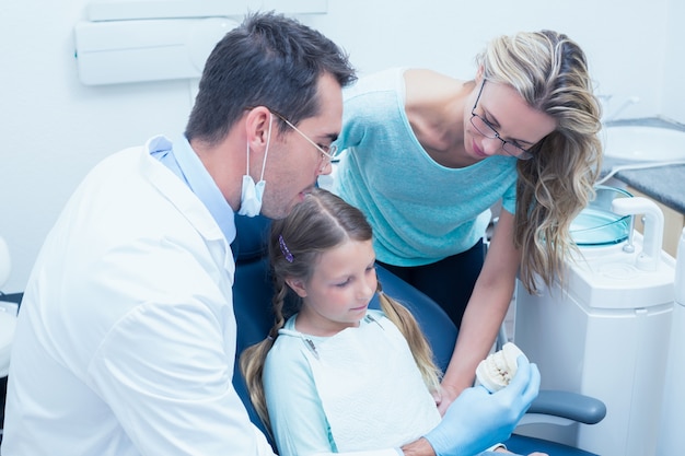 Dentista com assistente de ensinar garota como escovar os dentes