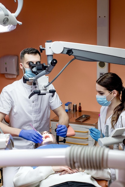 Dentista com assistente sob microscópio trata os dentes do paciente. odontologia progressiva moderna