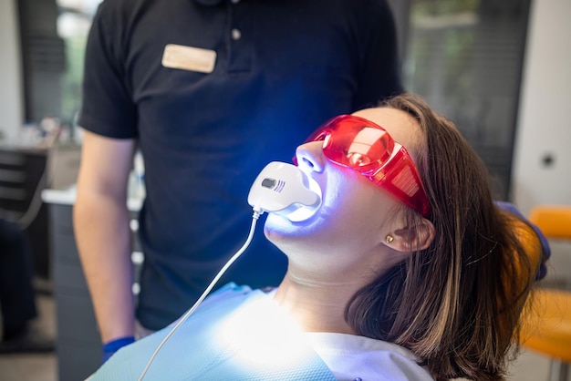 Dentista com um assistente de macacão usa lâmpadas UV durante o tratamento dos dentes de um paciente