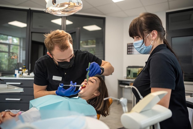 Dentista começa a verificar ou examinar o dente de uma jovem paciente deitada na cadeira odontológica