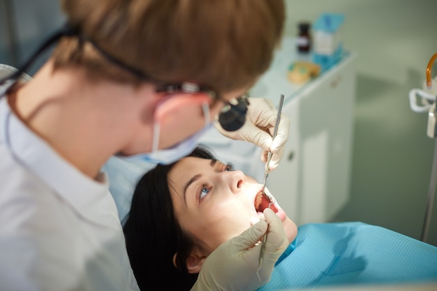 El dentista comienza a examinar la cavidad bucal de una niña hermosa.