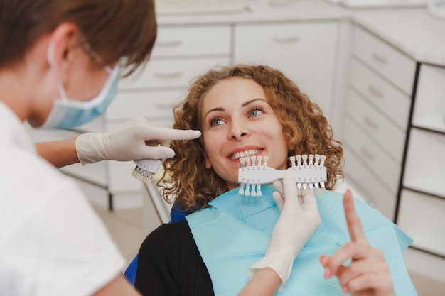 El dentista compara el color de los dientes del paciente con muestras para el tratamiento de blanqueamiento.