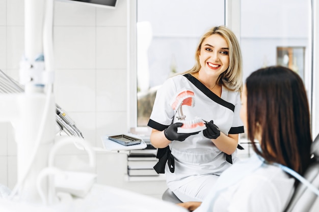 Dentista consideravelmente fêmea que explica a maneira de tratamento na dentadura para o paciente na clínica.