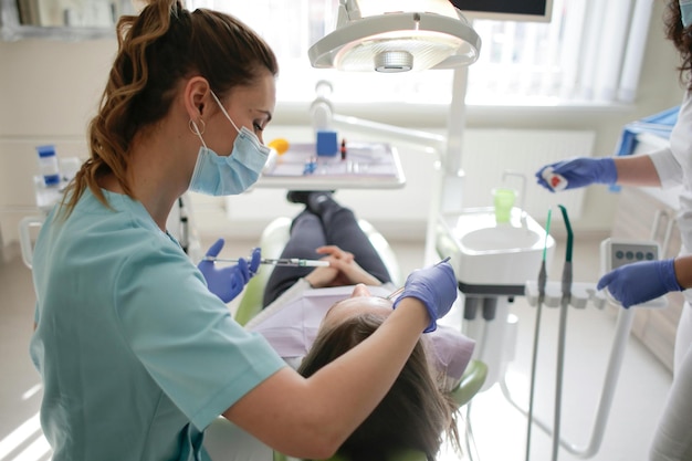Dentista en el consultorio dental hablando con una paciente femenina y preparándose para el tratamiento
