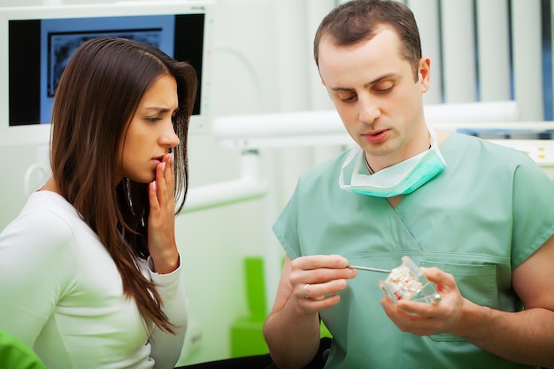 Dentista en el consultorio dental hablando con una paciente y preparándose para el tratamiento