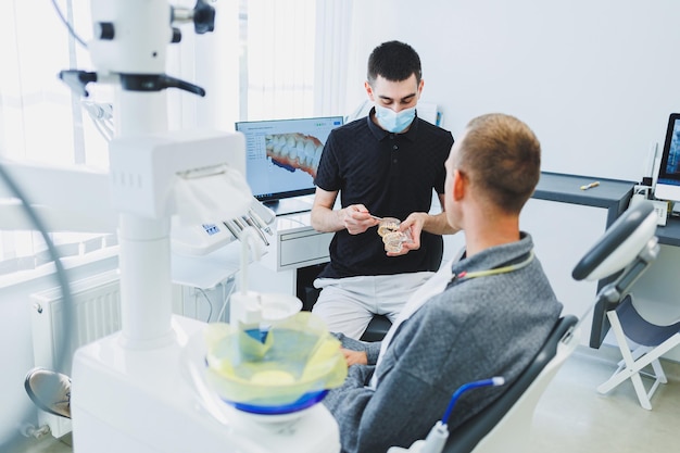 Un dentista en un consultorio dental moderno le cuenta a un paciente sobre el cuidado dental Un hombre se sienta en una silla dental y escucha a un dentista