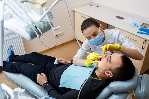 El dentista en el consultorio trata los dientes del paciente que está en el sillón dental. odontología. El dentista coloca un empaste dental en su paciente. Cuidado bucal. Foto de alta calidad