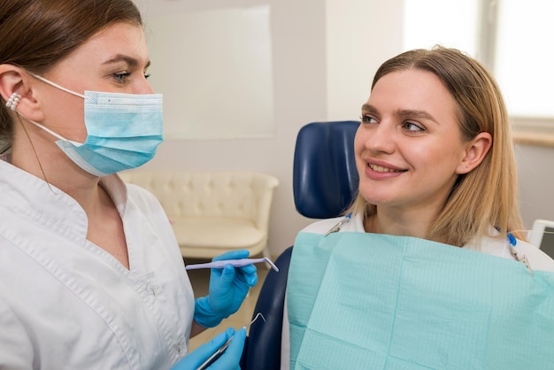 Dentista conversando com um clientevista lateral de uma dentista feminina dando conselhos e uma cliente feminina sentada em uma cadeira odontológica