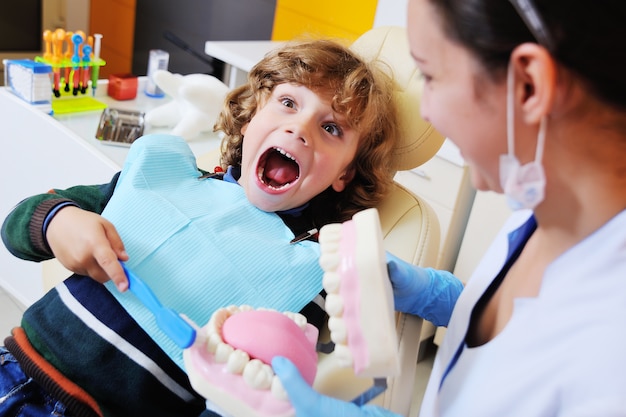 Foto el dentista le cuenta al niño sobre la higiene bucal y le muestra una mandíbula artificial y un cepillo de dientes.