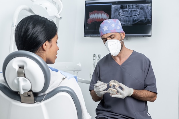 Dentista dando uma explicação a um paciente enquanto segura um molde plástico odontológico em uma clínica odontológica