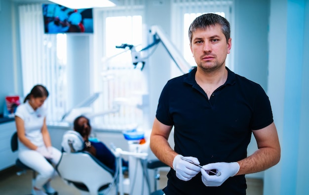 Dentista de camisa preta posa para a câmera a equipe médica está trabalhando no fundo estomatologia moderna odontologia