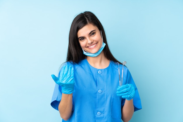 Dentista de jovem segurando ferramentas sobre parede azul isolada, convidando para vir