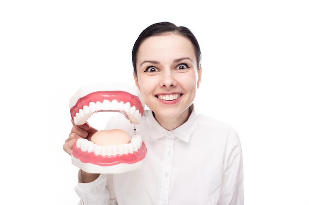 Foto dentista de mulher engraçada em uma camisa branca tem uma mandíbula grande com dentes nas mãos fundo branco