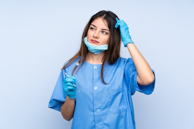 Dentista de mulher segurando ferramentas com dúvidas e com a expressão do rosto confuso
