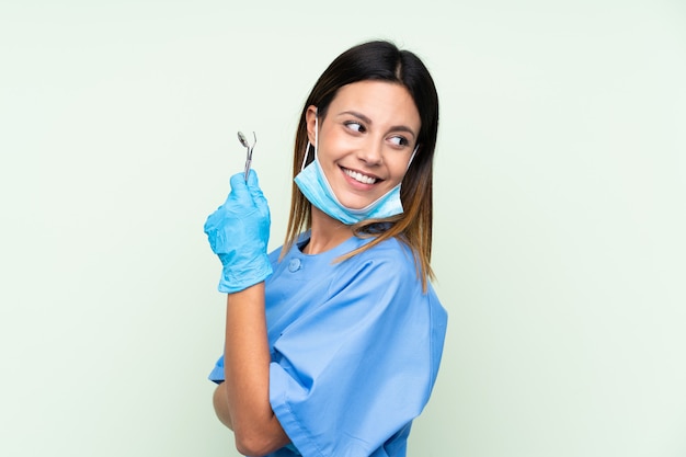 Dentista de mulher segurando ferramentas sobre isolado parede verde rindo